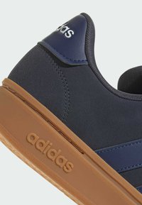 Gros plan sur le talon d'une basket Adidas bleu marine avec une semelle en gomme, le logo Adidas embossé sur la semelle et imprimé sur la languette arrière.