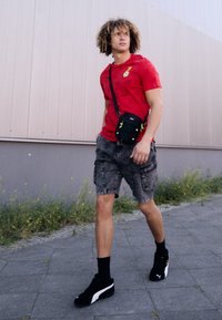 Rød t-shirt med korte ærmer og fodboldmotiv, grå cargo-shorts, sorte sneakers og en lille sort crossbody-taske med grønne detaljer.
