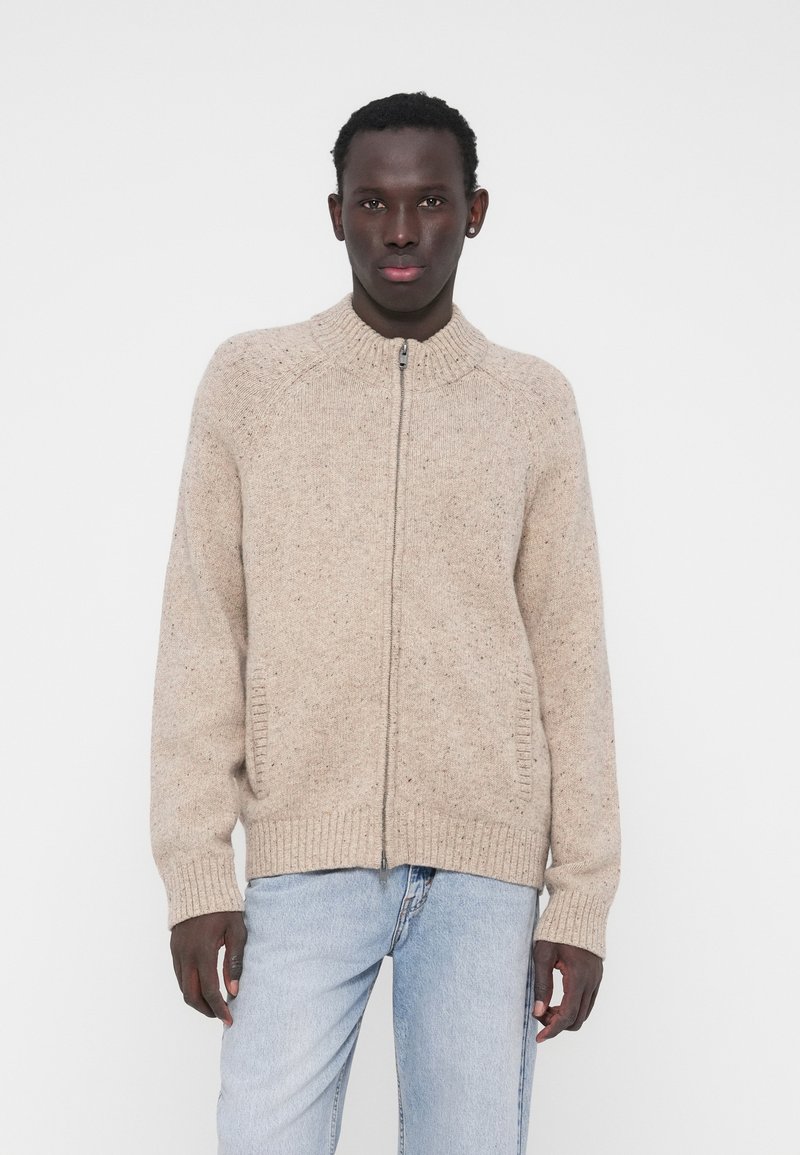 Beež värvliga lahtine kampsun kõrge kraega, soonikkoes varrukate ja alumise äärega. Valmistatud tekstuurse kudumiga kangast, millel on värvilised täpid. Kaasas küljetaskud.