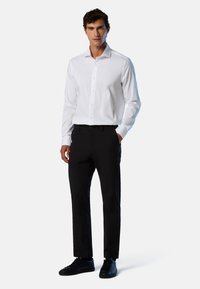 Weißes Langarmhemd mit strukturiertem Kragen, Knopfleiste, und schwarze Slim-Fit-Hose kombiniert mit schwarzen Sneakern. Minimalistisches Design.