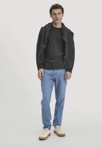 Schwarzer Kapuzenpullover, kombiniert mit hellblauen Jeans und cremefarbenen Sneakers. Das Outfit hat eine lässige Passform und ein schlichtes Design.