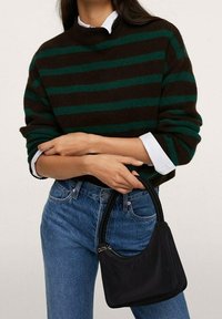 Pull tricoté rayé marron et vert avec un col montant, associé à un jean bleu clair, tenant un petit sac à main en cuir noir.