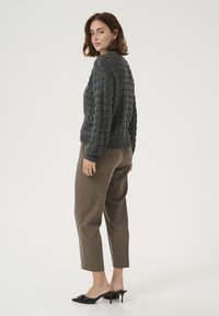 Maglione grigio lavorato a maglia con un motivo testurizzato, abbinato a pantaloni marroni a gamba affusolata e mule con tacco neri. L'outfit è semplice e informale.