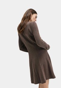 Brązowa sukienka z długim rękawem, dopasowanym korpusem i rozkloszowaną spódnicą, o gładkiej fakturze. Prosty design bez widocznych wzorów czy akcentów.