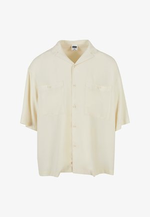 Kurzärmliges, lockeres Shirt aus cremefarbenem Stoff, mit Kragen, zwei Fronttaschen und Knopfverschluss vorne. Glatte Textur, minimales Design.