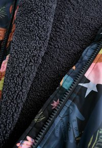 Tõmblukuga jope sisu, mis on pehme tumehallast fliisist, ja särava lillemustriga välimine pool erinevates värvides.