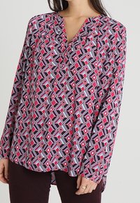 Långärmad blus i lätt tyg med ett geometriskt mönster av rosa, marinblå och vita diamanter. V-ringning med subtila veck.