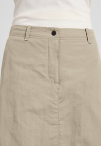 Gonna beige a taglio dritto, realizzata in tessuto leggero. Presenta una tasca frontale, cuciture a vista e un bottone nero in vita.
