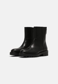 Černé kožené kotníkové boty s hladkým povrchem, bočním zipem a masivní gumovou podrážkou se zvýšenými vzory pro lepší trakci.