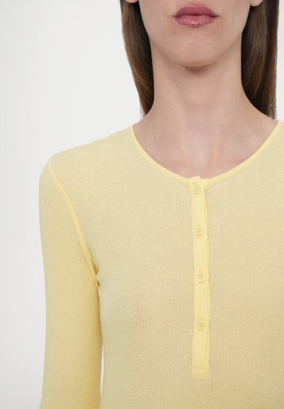 Yellow ribbed long-sleeve top with a round neckline and six button placket. Soft fabric with a textured finish, fitted style.