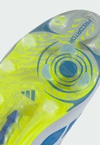 Gros plan sur la semelle d'une chaussure de football jaune néon et bleue avec des crampons transparents et des éléments de traction circulaires étiquetés "Predator".