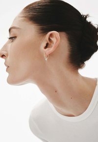 Pendiente de aro plateado exhibido en la oreja de un modelo, con una forma redonda simple y un acabado pulido. La piel parece lisa y tensa.