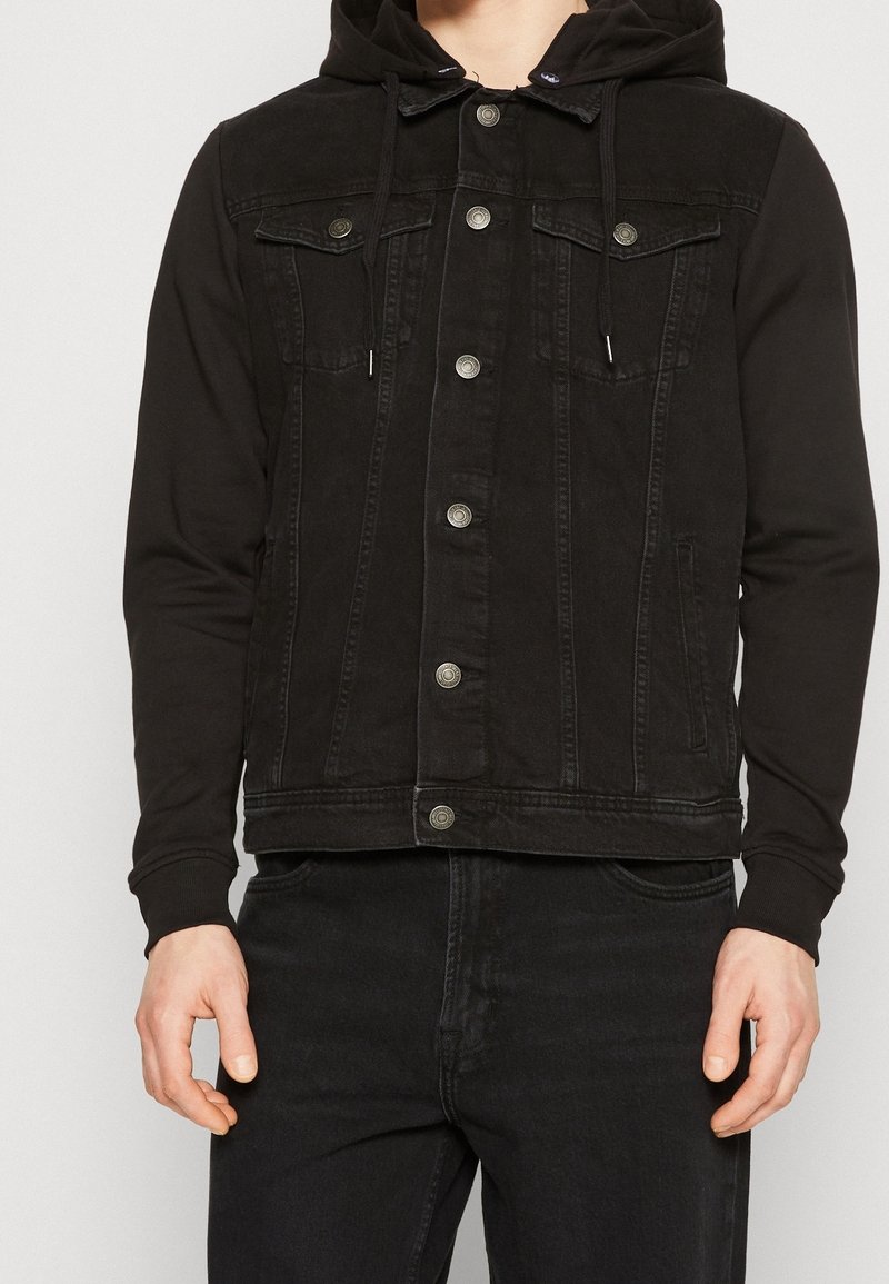 Svart denimjacka med huva, utrustad med knäppningar, bröstfickor och en kontrasterande tygtextur från ärmarna.