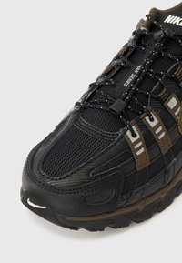 Juodi ir rudi Nike bėgimo bateliai su tinklinio audinio viršumi, reguliuojamais elastingais raišteliais ir prekės ženklo audiniais ženkliukais šonuose.