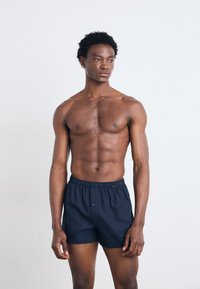 Boxers en coton navy avec une taille élastique, fermeture à bouton unique et une texture légère, présentés sur un mannequin masculin.