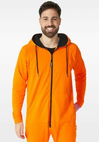 Oranžová mikina na zip s černou kapucí, disponující přední kapsou, šňůrkami a texturovanou látkou. Přiléhavý design s dlouhými rukávy.