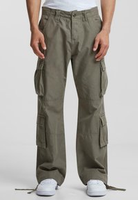 Pantaloni cargo din bumbac de culoare verde măslin, cu mai multe buzunare laterale, o croială relaxată și crampe ajustabile la tiv. Purtați cu adidași albi.