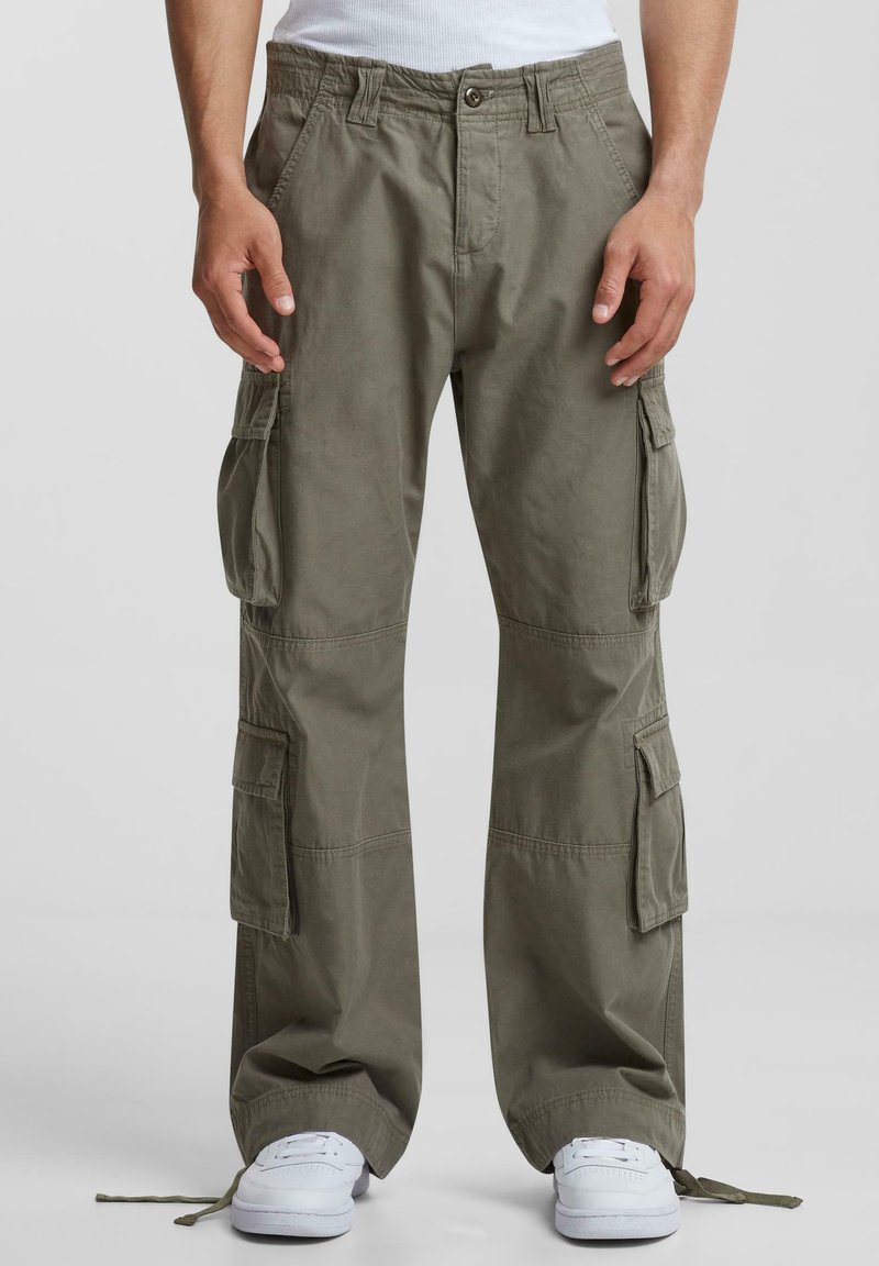 Pantaloni cargo din bumbac de culoare verde măslin, cu mai multe buzunare laterale, o croială relaxată și crampe ajustabile la tiv. Purtați cu adidași albi.