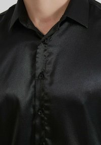 Chemise en satin noir avec une texture lisse, dotée d'un col, de boutons sur le devant et d'une finition brillante.