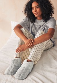 Chaussons en fausse fourrure bleu clair doux avec une texture pelucheuse et un design montants, associés à un pantalon de pyjama crème à rayures.