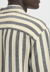 Camicia a righe con strisce verticali alternate blu navy e crema, dettagliata con un colletto classico e un leggero tessuto texturizzato.