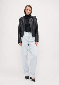 Black faux leather bomber jacket with a zip front, fitted silhouette, and long sleeves, paired with light blue loose-fit jeans and black heels.