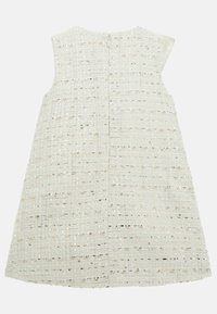 Witte mouwloze jurk van textuurstof met een geweven patroon en subtiele metallic draden; voorzien van een centrale rits aan de achterkant.