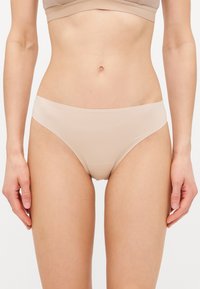 Lichtbeige bikini ondergoed gemaakt van glad, rekbaar materiaal met een laag uitgesneden ontwerp en naadloze randen. Geen zichtbare patronen of hardware.