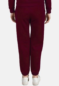 Bordeaux joggerbroeken met een zachte textuur, elastische boorden en een relaxte pasvorm, gecombineerd met witte sneakers voor casual draag.
