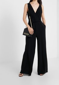 Mono negro con un escote en V profundo, piernas anchas y cintura ceñida. Combinado con un pequeño bolso negro con herrajes en dorado.