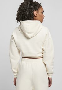 Avkortet kremfarget hettegenser med hette og vide ermer, laget av mykt stoff. Elastisk midjebånd på matchende joggebukser. Minimalistisk design.