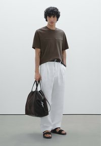 T-shirt marrone a maniche corte, pantaloni bianchi plissettati, cintura nera, borsa a tracolla marrone scuro con zip argentata e sandali neri.