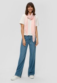 Lichtroze sjaal met franjes gedragen over een witte t-shirt, gecombineerd met lichtblauwe wijde jeans en witte sneakers.