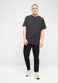 Camiseta de algodón gris con un corte relajado, mangas cortas y escote redondo, combinada con pantalones negros ajustados y zapatillas beige.