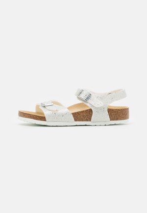 Sølvglitrende sandal med åben tå med to justerbare remme og en korkfodsål på en hvid baggrund.