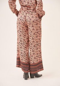 Pantalones de pierna ancha con estampado de flores en rosa claro, con un dobladillo de patrón en contraste. Cuentan con una cinturilla elástica y una tela ligera y fluida.