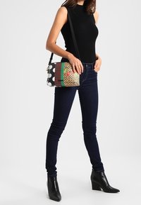 Multifarvet crossbody taske med prikker, vævede mønstre og blomsterdetaljer, med en glat overflade og justerbar rem.