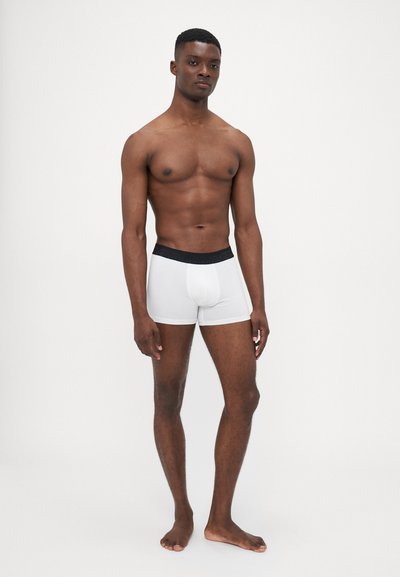 Hvide boxer shorts med en sort elastisk talje, vist på en model med en glat tekstur og tætsiddende design.