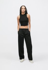 Čierny crop top a čierne voľné teplákové nohavice s postrannými vreckami a bielymi pruhmi na bokoch. Model stojí na svetlom pozadí.