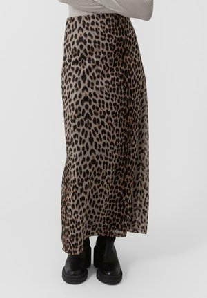 Jupe maxi en imprimé léopard en tissu léger, présentant un design taille haute et une fente sur le côté. Portée avec des bottes noires à semelles épaisses.