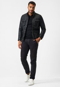 Svart läderjacka med två framfickor, kombinerad med en svart tröja, mörka byxor och vita sneakers. Enkel, åtsittande design.