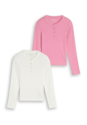 Due maglie Henley a maniche lunghe con patta di bottoni, una bianca e una rosa, esposte distese su sfondo bianco.