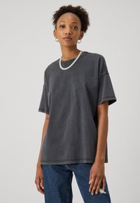 Dunkelgraues, oversized T-Shirt aus Baumwolle mit Rundhalsausschnitt und kurzen Ärmeln. Mit ausgefransten Details und sichtbaren Nähten.