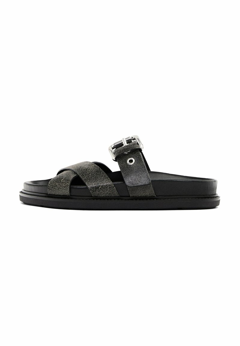 Sandale slide en cuir noir avec des brides croisées et une boucle métallique ajustable sur une semelle épaisse.