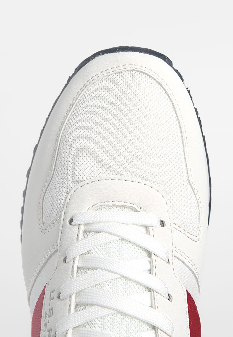 Scarpa atletica bianca con una tomaia testurizzata, dettagli rossi e suola in gomma. Presenta lacci bianchi e un design cucito lungo i bordi.