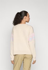 Cremfarbener gestrickter Pullover mit lockerer Passform, der pastellfarbene geometrische Muster an den Ärmeln aufweist. Weiche Textur und geribberter Saum.