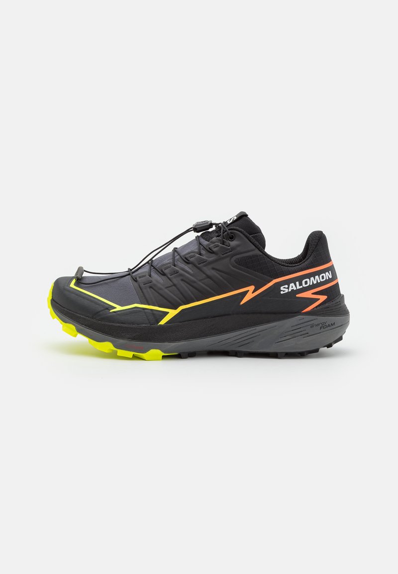 Zapatilla de trail running negra con acentos en amarillo y naranja, parte superior sintética, suela resistente y un sistema de cordones rápidos para un ajuste seguro.