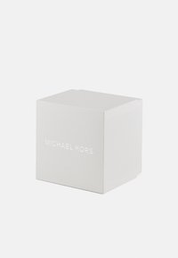 Caja de regalo de cartón blanco con un acabado texturizado; presenta el nombre de la marca "MICHAEL KORS" en letras plateadas en relieve en un lado.