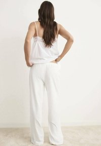 Top blanco con detalles de encaje en la parte de atrás, combinado con pantalones blancos holgados. Textura suave con una silueta relajada.