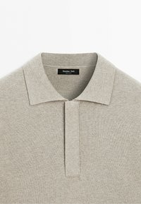Light beige knit polo shirt with a soft collar and concealed button placket, featuring a Massimo Dutti label inside the neck.